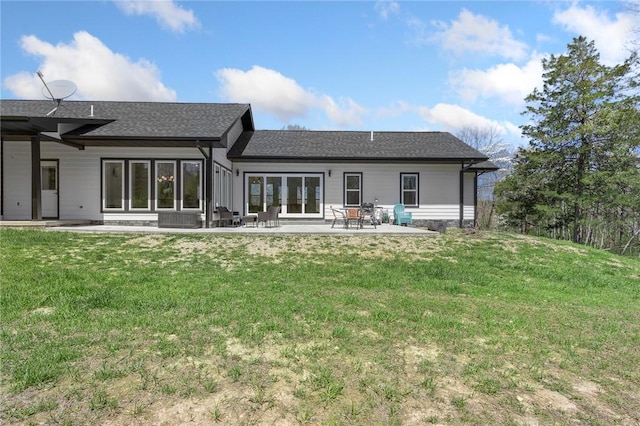 back of property with a shingled roof, a yard, and a patio