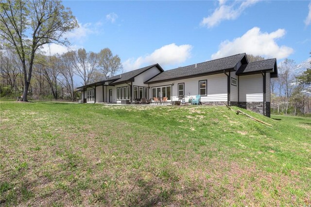 back of property with a lawn, a shingled roof, and a patio