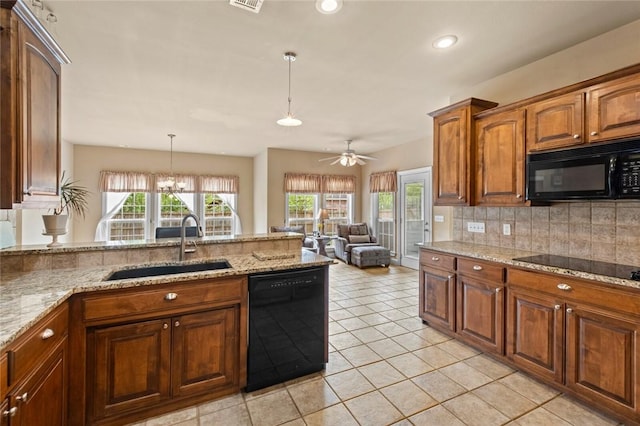 kitchen with a sink, light stone countertops, decorative backsplash, black appliances, and hanging light fixtures