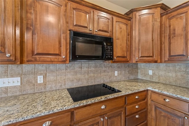 kitchen with light stone countertops, brown cabinetry, backsplash, and black appliances