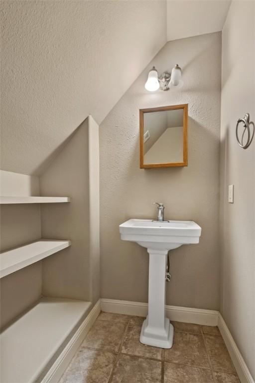 bathroom featuring lofted ceiling, baseboards, a textured ceiling, and tile patterned flooring