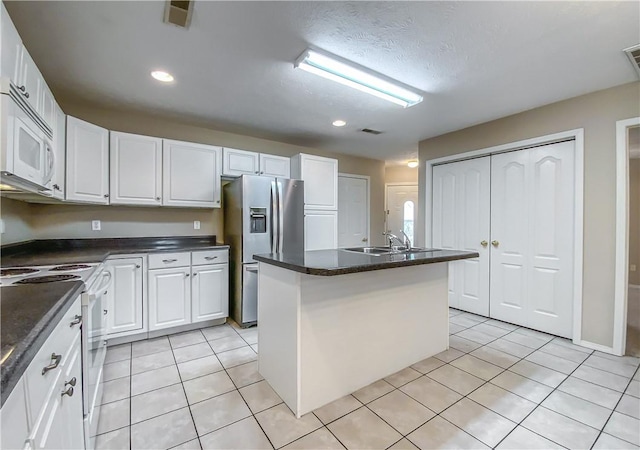 kitchen with dark countertops, a sink, white appliances, white cabinetry, and visible vents
