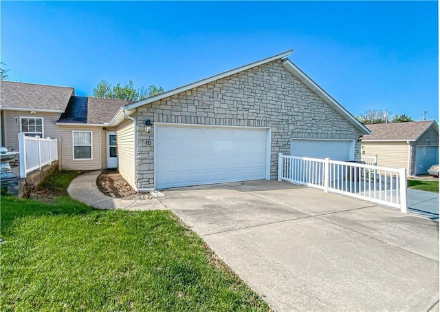 view of front of property with a front lawn, stone siding, a shingled roof, fence, and a garage