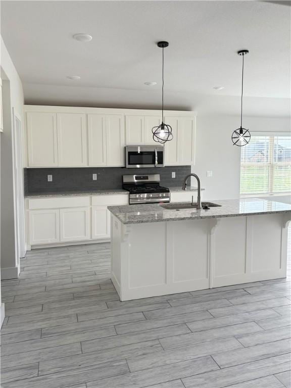 kitchen featuring light stone counters, stainless steel appliances, backsplash, a sink, and white cabinetry