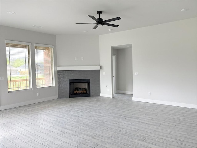 unfurnished living room featuring a fireplace, wood finished floors, baseboards, and ceiling fan