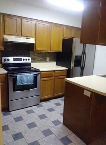 kitchen featuring stainless steel appliances, under cabinet range hood, light countertops, light floors, and tasteful backsplash