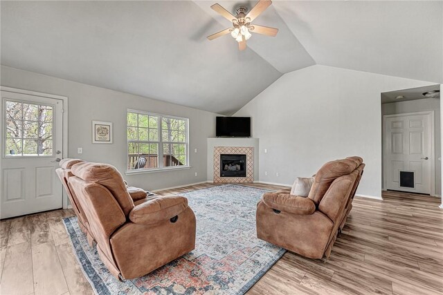 living area with a tile fireplace, lofted ceiling, light wood finished floors, a ceiling fan, and baseboards