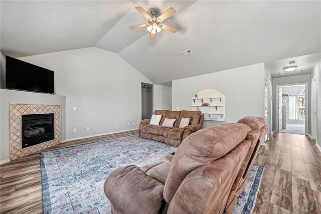 living area featuring lofted ceiling, wood finished floors, visible vents, a fireplace, and ceiling fan