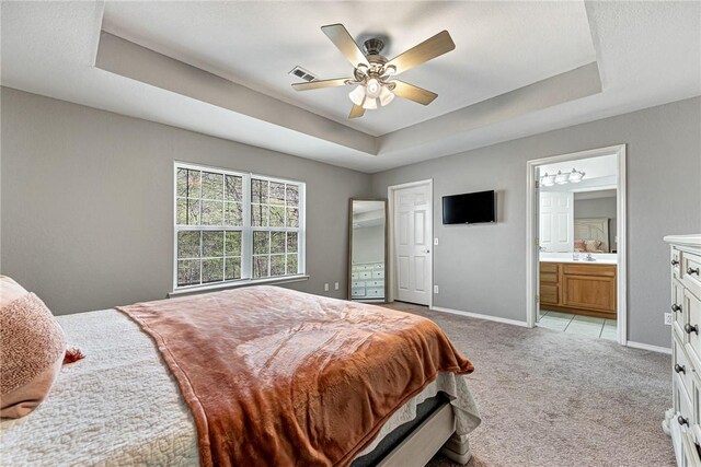 bedroom with light carpet, visible vents, baseboards, connected bathroom, and a raised ceiling