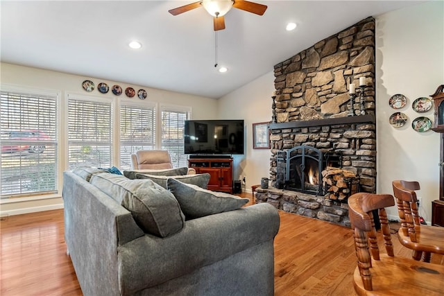 living area with vaulted ceiling, a stone fireplace, wood finished floors, baseboards, and ceiling fan