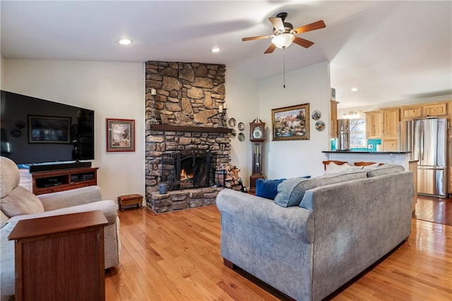 living area featuring a fireplace, light wood-style floors, vaulted ceiling, and a ceiling fan