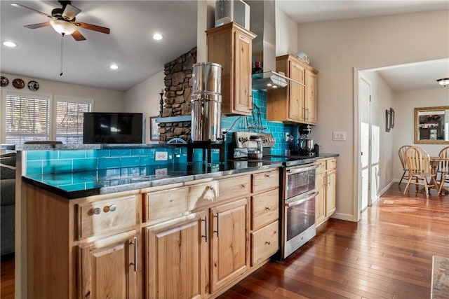 kitchen with decorative backsplash, light brown cabinetry, double oven range, wall chimney exhaust hood, and dark wood-style floors