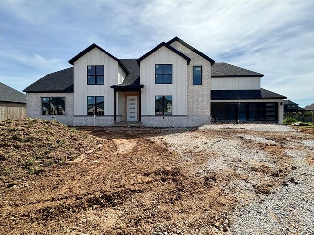 modern farmhouse style home featuring brick siding, board and batten siding, and roof with shingles