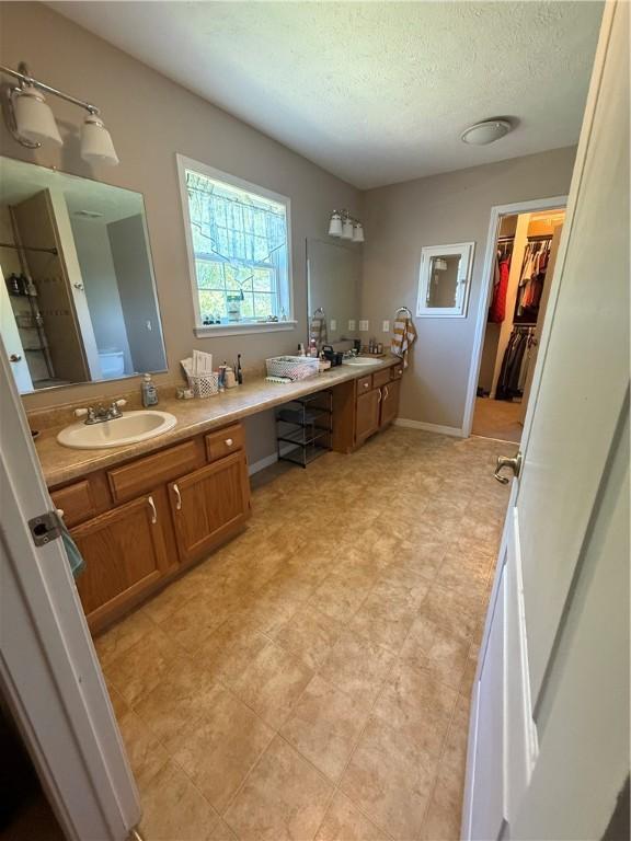 1306 Sunset Blvd, Berryville, AR 72616 - bathroom featuring a textured ceiling, double vanity, a spacious closet, and a sink