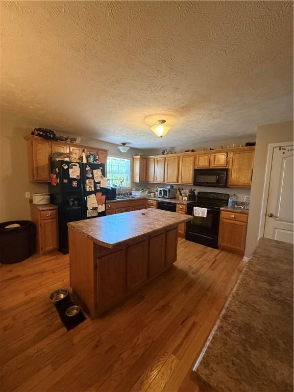 1306 Sunset Blvd, Berryville, AR 72616 - kitchen featuring light wood finished floors, a sink, a textured ceiling, a kitchen island, and black appliances