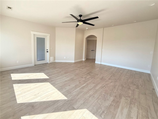 empty room featuring ceiling fan, arched walkways, light wood-style flooring, baseboards, and visible vents