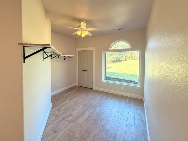interior space featuring baseboards, a ceiling fan, light wood-style flooring, and visible vents