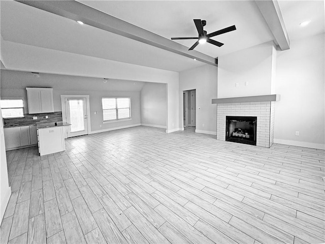 unfurnished living room featuring light wood-type flooring, baseboards, beam ceiling, and ceiling fan