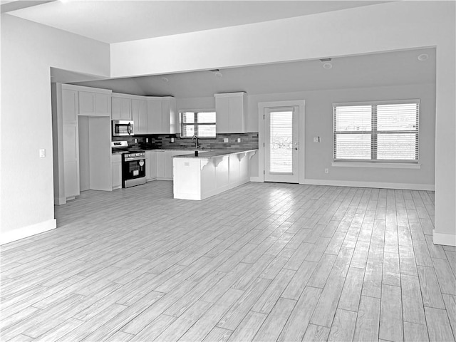 kitchen with stainless steel appliances, a sink, baseboards, open floor plan, and white cabinetry