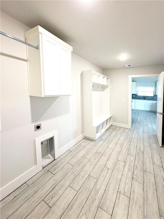 laundry area featuring visible vents, baseboards, electric dryer hookup, cabinet space, and light wood-style flooring