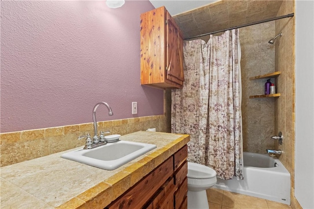 full bath featuring tile patterned floors, toilet, shower / tub combo with curtain, a textured wall, and vanity