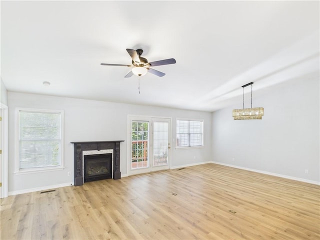unfurnished living room with baseboards, ceiling fan with notable chandelier, and light wood-style flooring