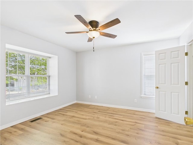 spare room featuring baseboards, a ceiling fan, visible vents, and light wood finished floors