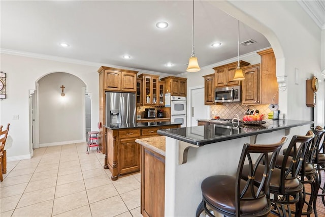 17444 16th Hwy, Siloam Springs, AR 72761 - kitchen featuring appliances with stainless steel finishes, arched walkways, brown cabinetry, a peninsula, and decorative backsplash