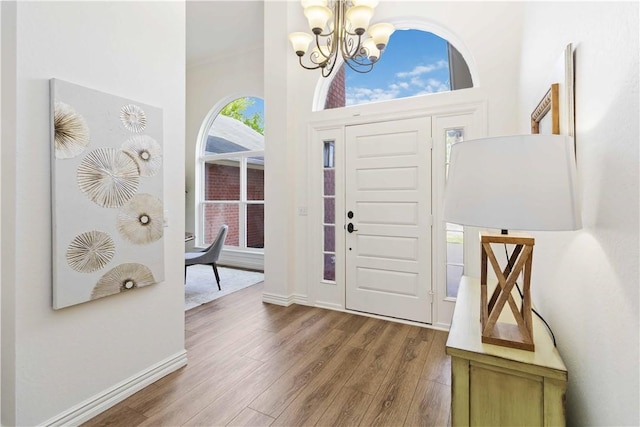 foyer with baseboards, wood finished floors, a high ceiling, and a chandelier