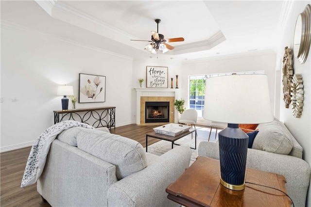 living area with a tray ceiling, wood finished floors, crown molding, a tiled fireplace, and ceiling fan