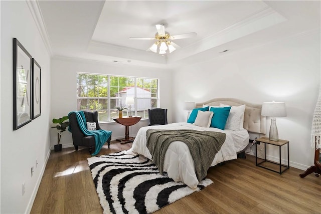 bedroom featuring a tray ceiling, wood finished floors, ornamental molding, baseboards, and ceiling fan