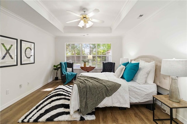 bedroom with a raised ceiling, wood finished floors, crown molding, and baseboards