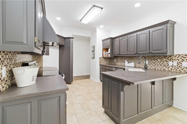 kitchen with a peninsula, a sink, backsplash, gray cabinets, and a breakfast bar area