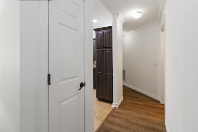 corridor featuring light wood-type flooring, baseboards, ornamental molding, and visible vents
