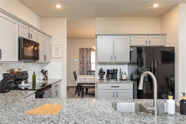 kitchen with black appliances, decorative backsplash, light stone counters, and a sink