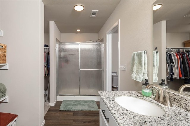 bathroom with wood finished floors, a stall shower, a walk in closet, vanity, and visible vents