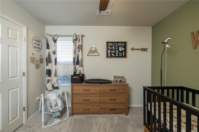 carpeted bedroom with visible vents, a crib, baseboards, and a ceiling fan