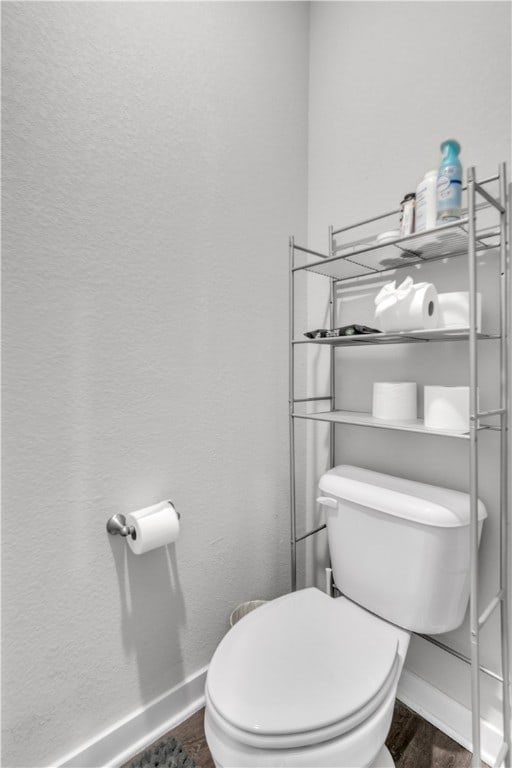 bathroom with a textured wall, wood finished floors, baseboards, and toilet