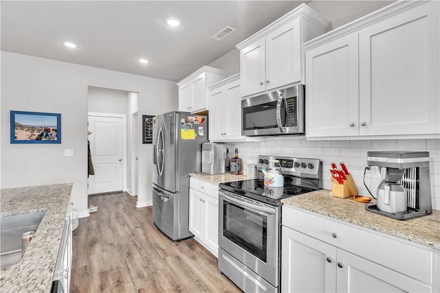 kitchen with white cabinets, light wood finished floors, stainless steel appliances, backsplash, and visible vents