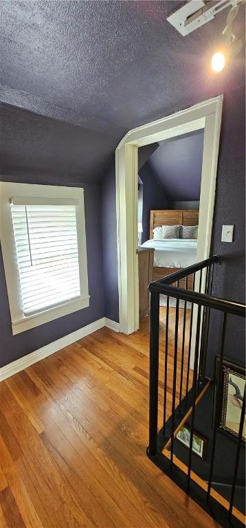 interior space featuring a textured ceiling, vaulted ceiling, baseboards, an upstairs landing, and wood finished floors