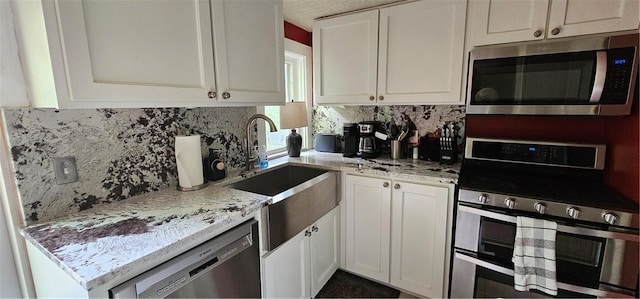 kitchen featuring light stone counters, backsplash, a sink, appliances with stainless steel finishes, and white cabinetry
