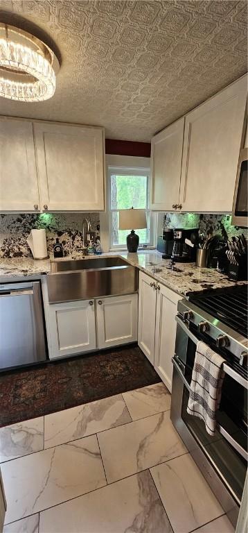kitchen with white cabinets, marble finish floor, stainless steel appliances, a sink, and light stone countertops