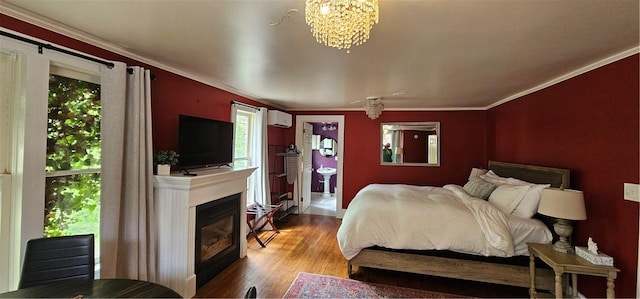 bedroom with an AC wall unit, a glass covered fireplace, a notable chandelier, wood finished floors, and crown molding