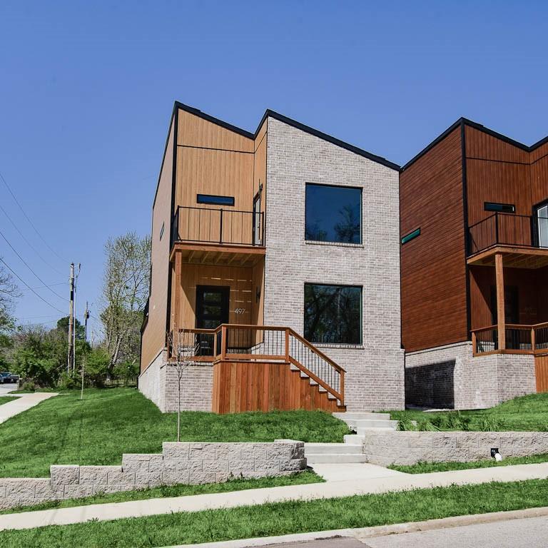 modern home featuring a front yard, a balcony, and brick siding