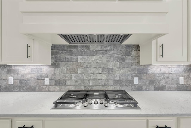 kitchen featuring stainless steel gas cooktop, white cabinets, tasteful backsplash, and custom range hood