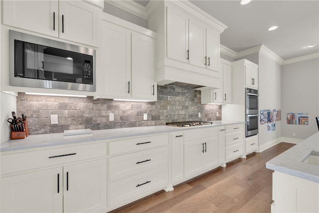 kitchen featuring light wood finished floors, stainless steel appliances, white cabinets, baseboards, and crown molding