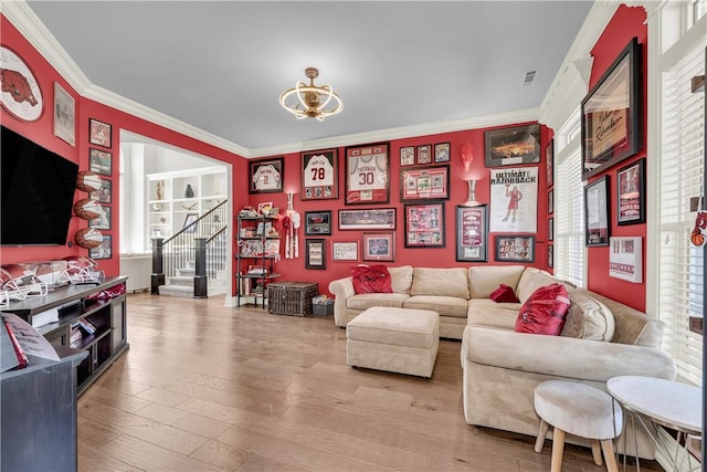 living area with plenty of natural light, stairway, an inviting chandelier, wood finished floors, and crown molding
