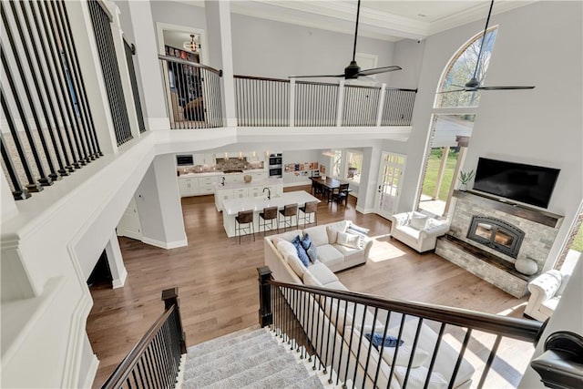 living room featuring wood finished floors, a high ceiling, ceiling fan, a fireplace, and ornamental molding