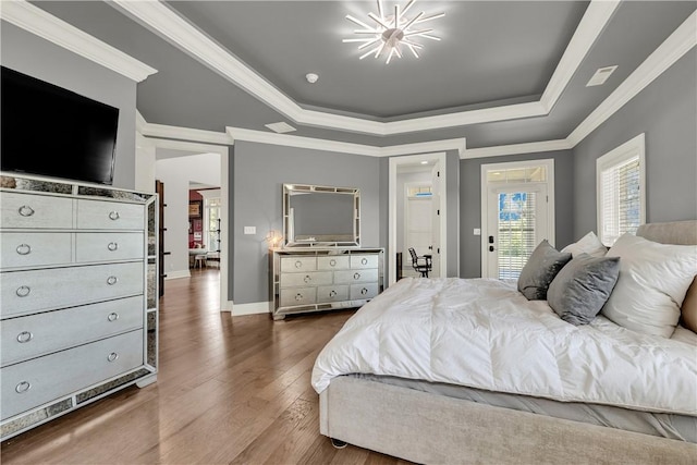 bedroom featuring ornamental molding, a chandelier, wood finished floors, and a raised ceiling