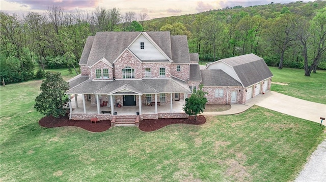 view of front of house featuring a wooded view, concrete driveway, a front lawn, a porch, and brick siding